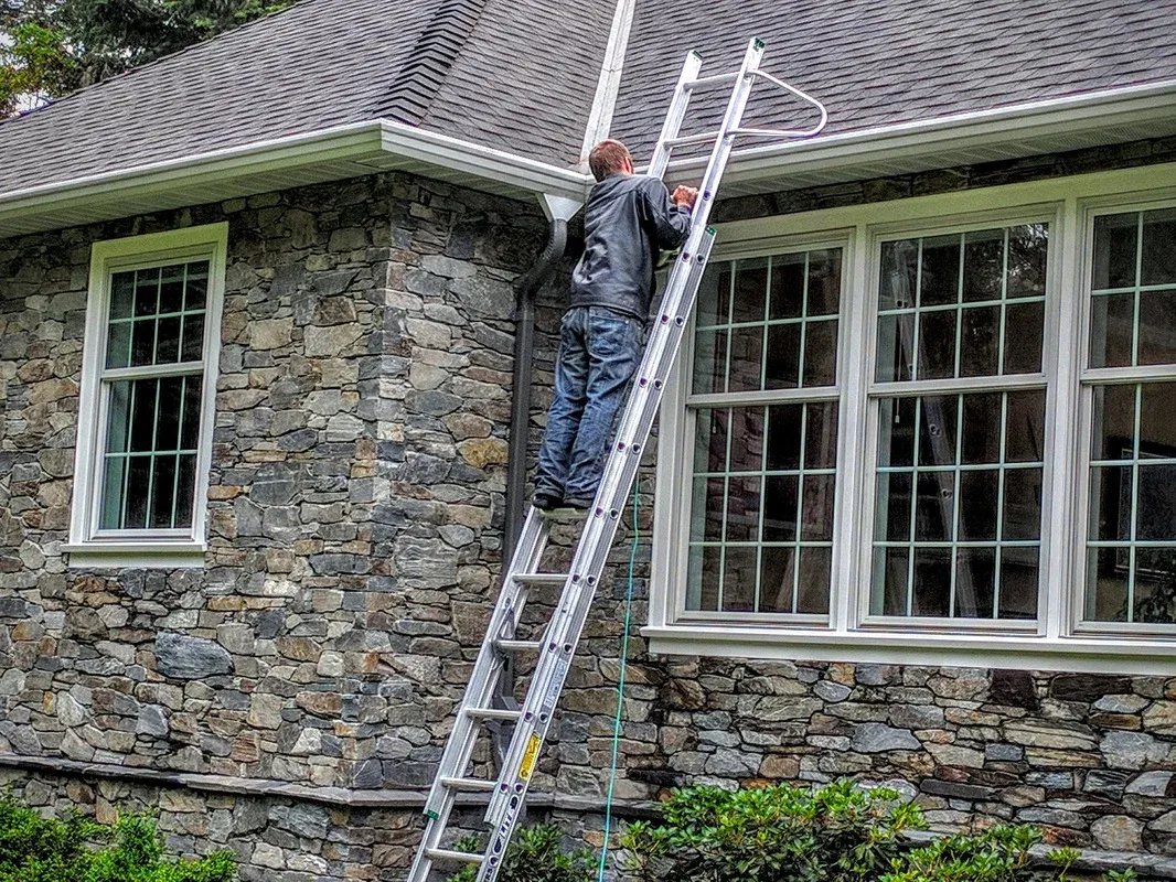 A ladder set at the eave of a house with the gutter line running away from it